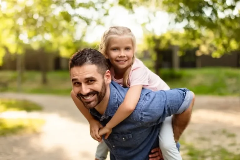 Happy father giving his daughter a piggyback ride outdoors, symbolizing the energy and vitality supported by Hormone Replacement Therapy