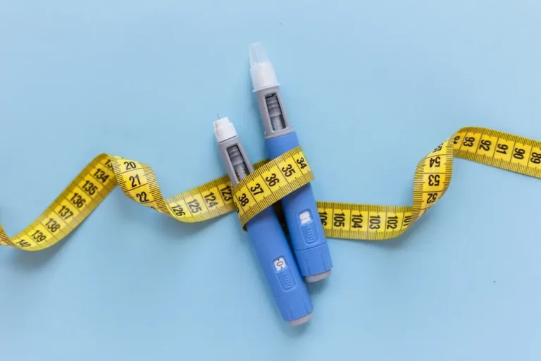Two hormone therapy pens wrapped with a yellow measuring tape on a blue background, symbolizing HRT weight loss and its effectiveness in managing weight.