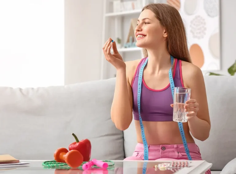 Hormonal Balance for Weight Loss is key to achieving sustainable fitness goals. A smiling woman in athletic wear sits on a couch, holding a glass of water and a supplement. A measuring tape hangs around her neck, symbolizing her focus on fitness and hormonal balance for weight loss. Healthy foods and fitness accessories are placed in front of her.