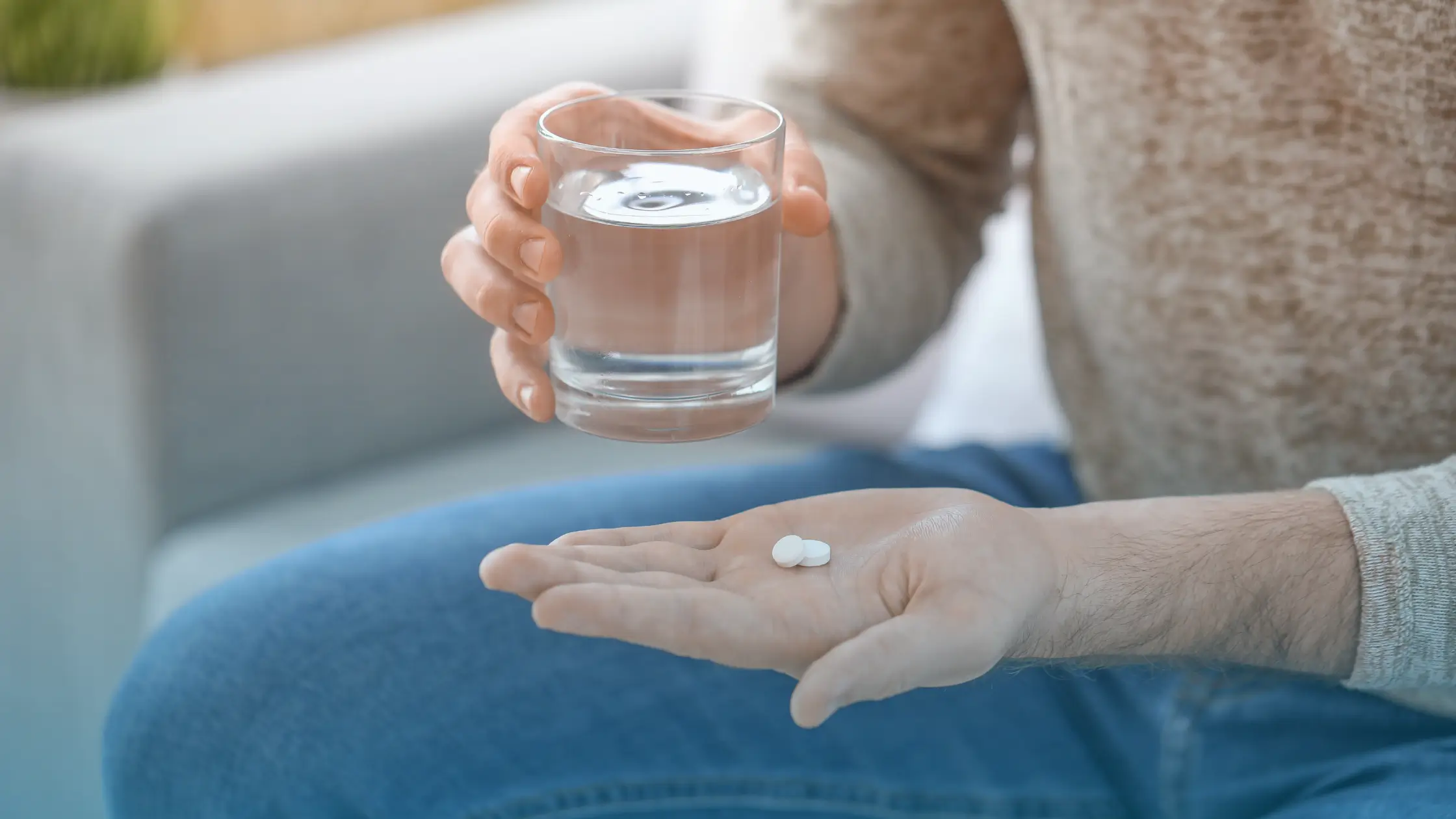 Man holding a pill in one hand and a glass of water in the other before taking modafinil tablets