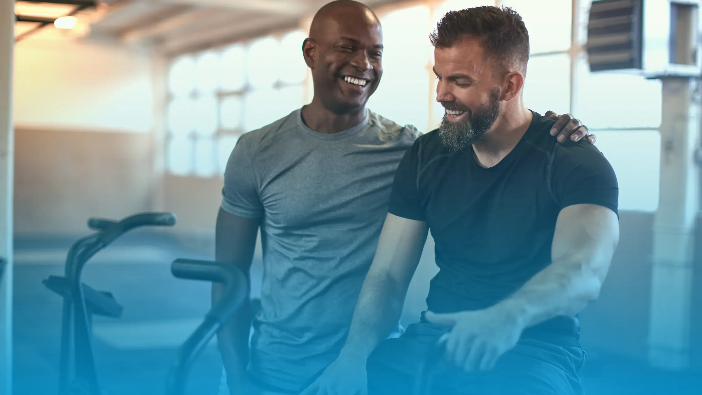 Two men smiling and talking in a gym after a workout, representing improved energy, confidence, and wellbeing during TRT treatment.
